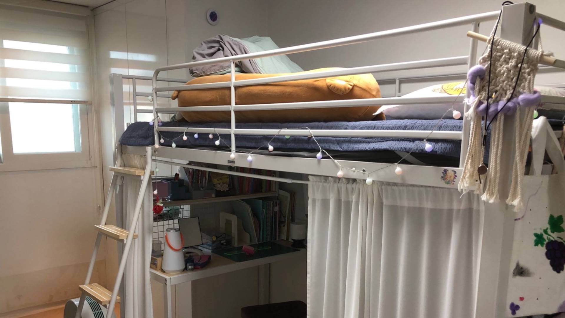 오른편에 철제 프레임으로 만든 2층 침대가 있다. 1층 공간에는 흰색 커튼이 달려 있고, 2층에는 여러 가지 침구가 있다. 1층과 2층은 사다리로 연결된다.
