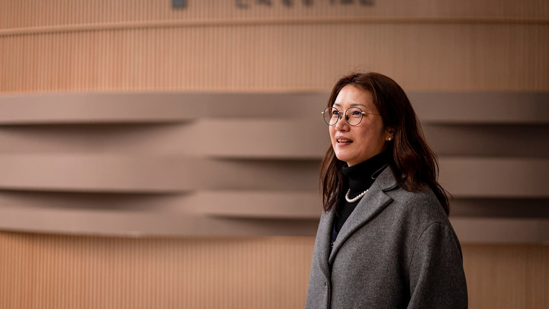 검정색 셔츠와 회색 코트를 입고 진주 목걸이를 한 지선씨가 살짝 웃고 있다.