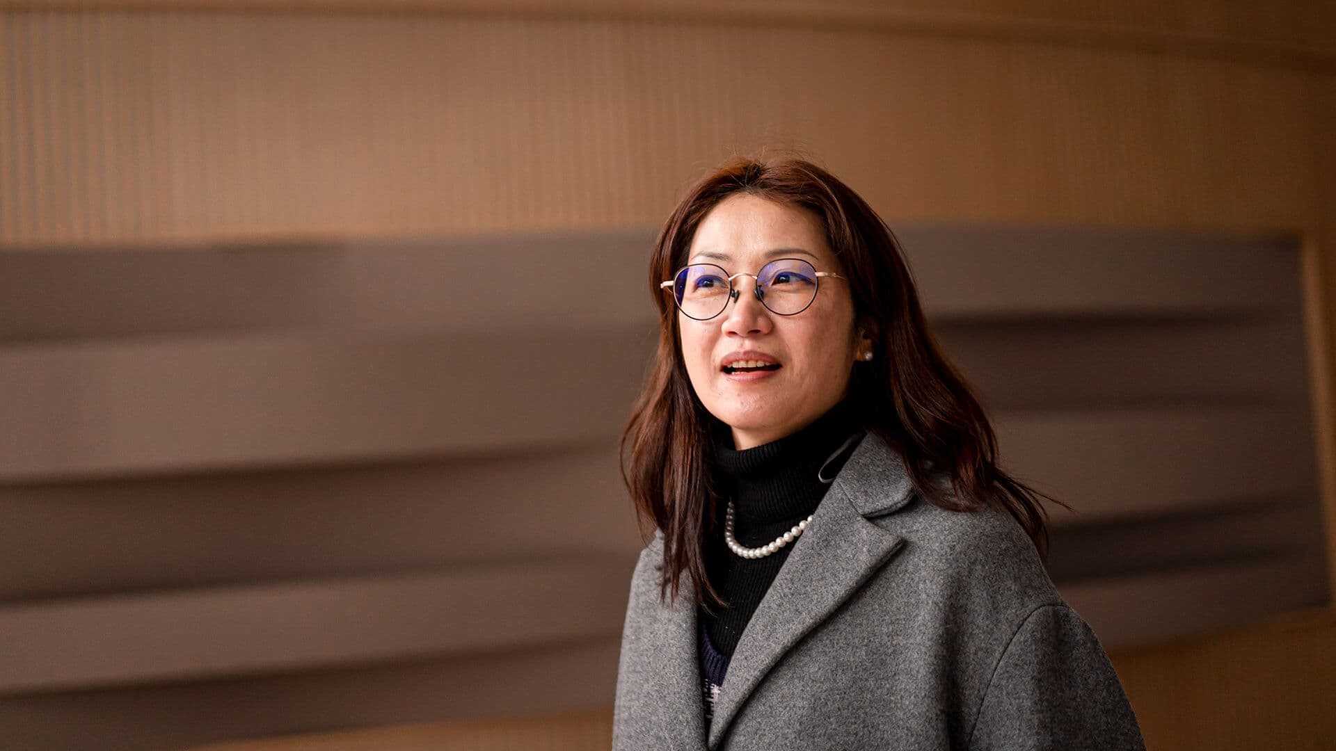 검정색 셔츠와 회색 코트를 입고 진주 목걸이를 한 지선씨가 살짝 웃고 있다.