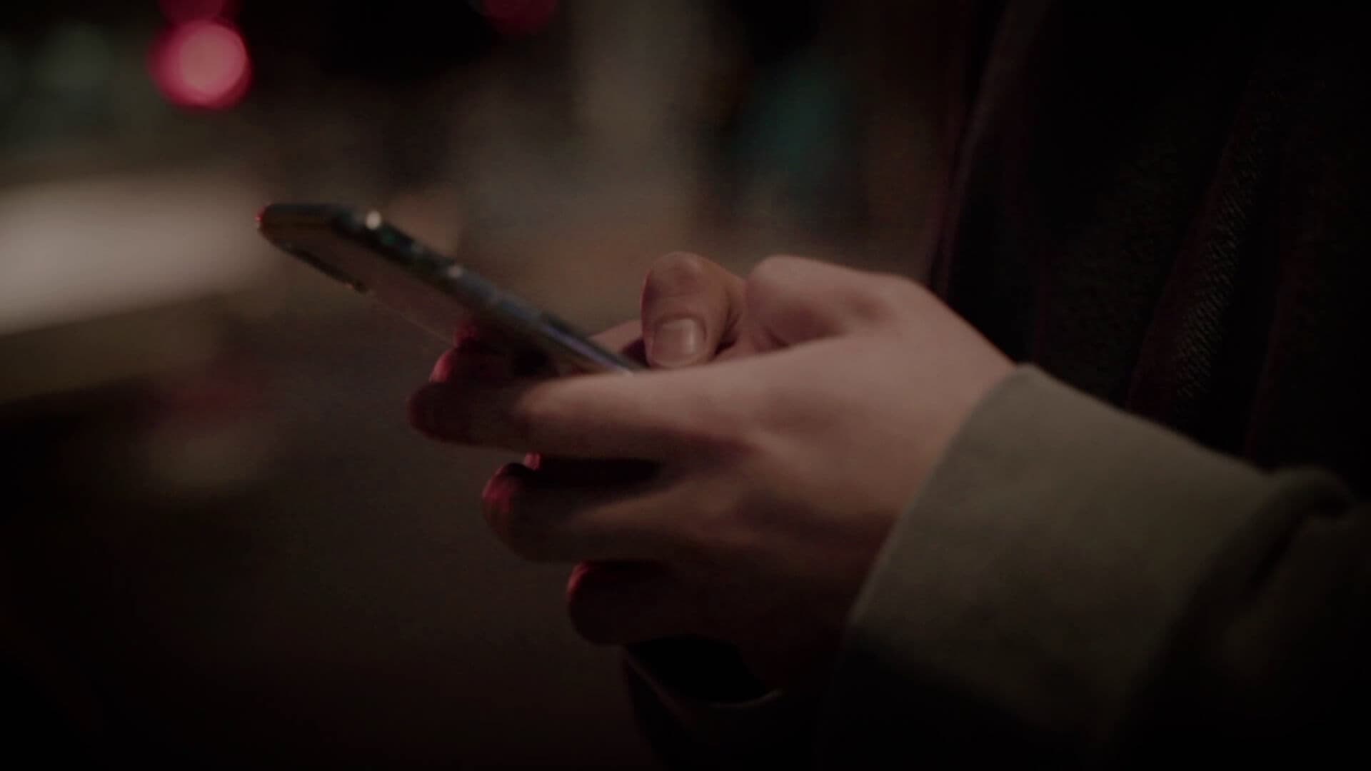 한 사람이 길거리에서 휴대폰을 두 손으로 잡고 있다.