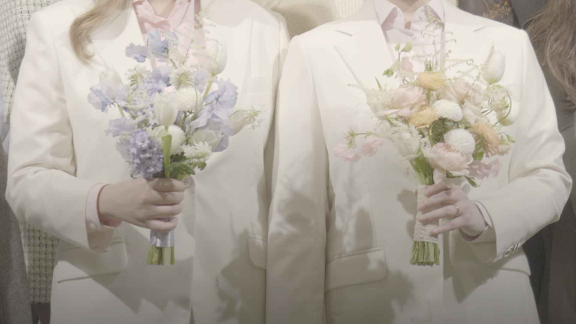 결혼식 당일의 모습이다. 수영과 지한 커플이 흰색 슈트를 입고, 각각 연보라색과 분홍색 위주로 구성된 꽃다발을 들고 서 있다.