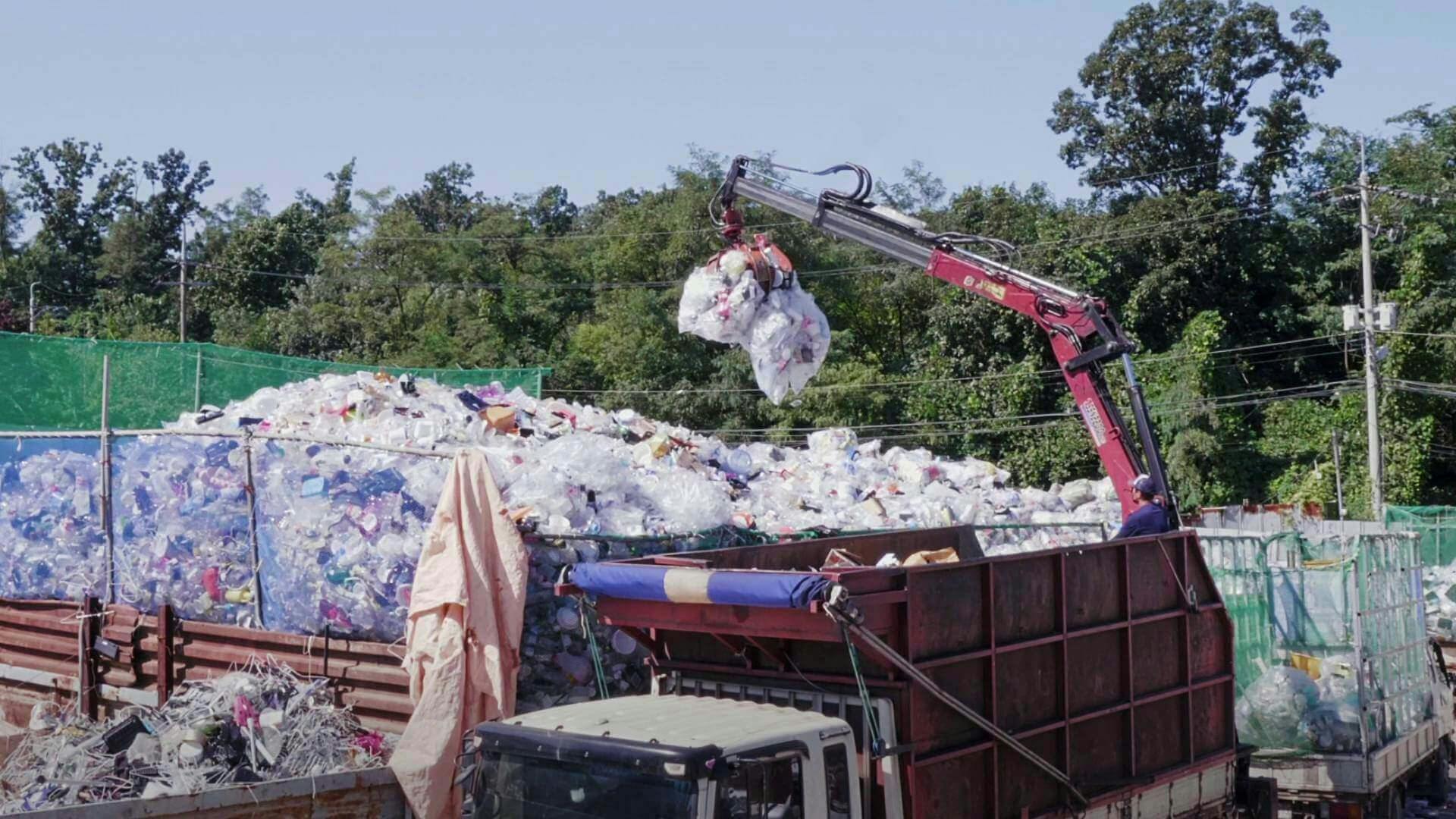 산처럼 쌓인 대형 쓰레기 봉투의 산 위에 빨간 포클레인이 쓰레기 봉투를 두 개 더 올리고 있다.