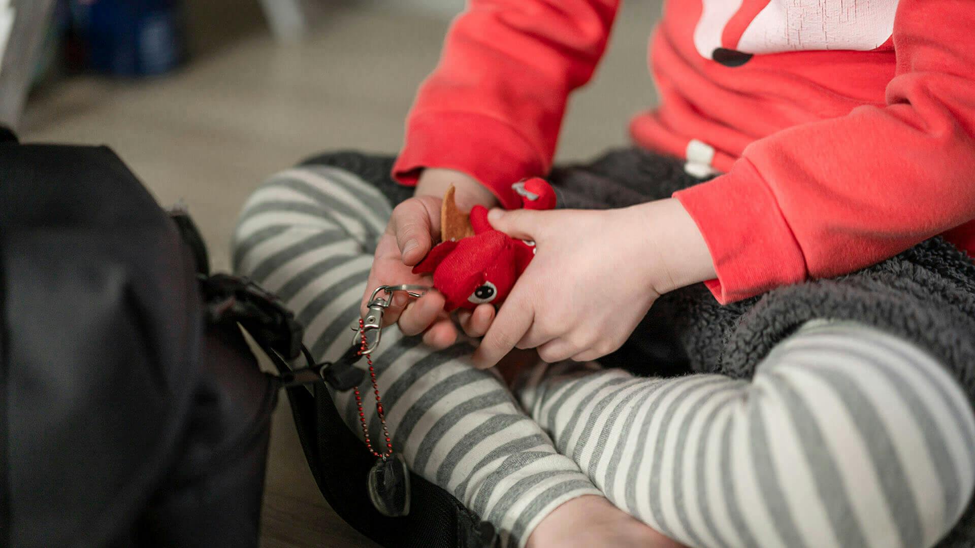 보영씨의 아이. 바닥에 앉아 장난감을 손에 쥐고 있다. 빨간색 셔츠, 얼룩무늬 바지를 착용했다.