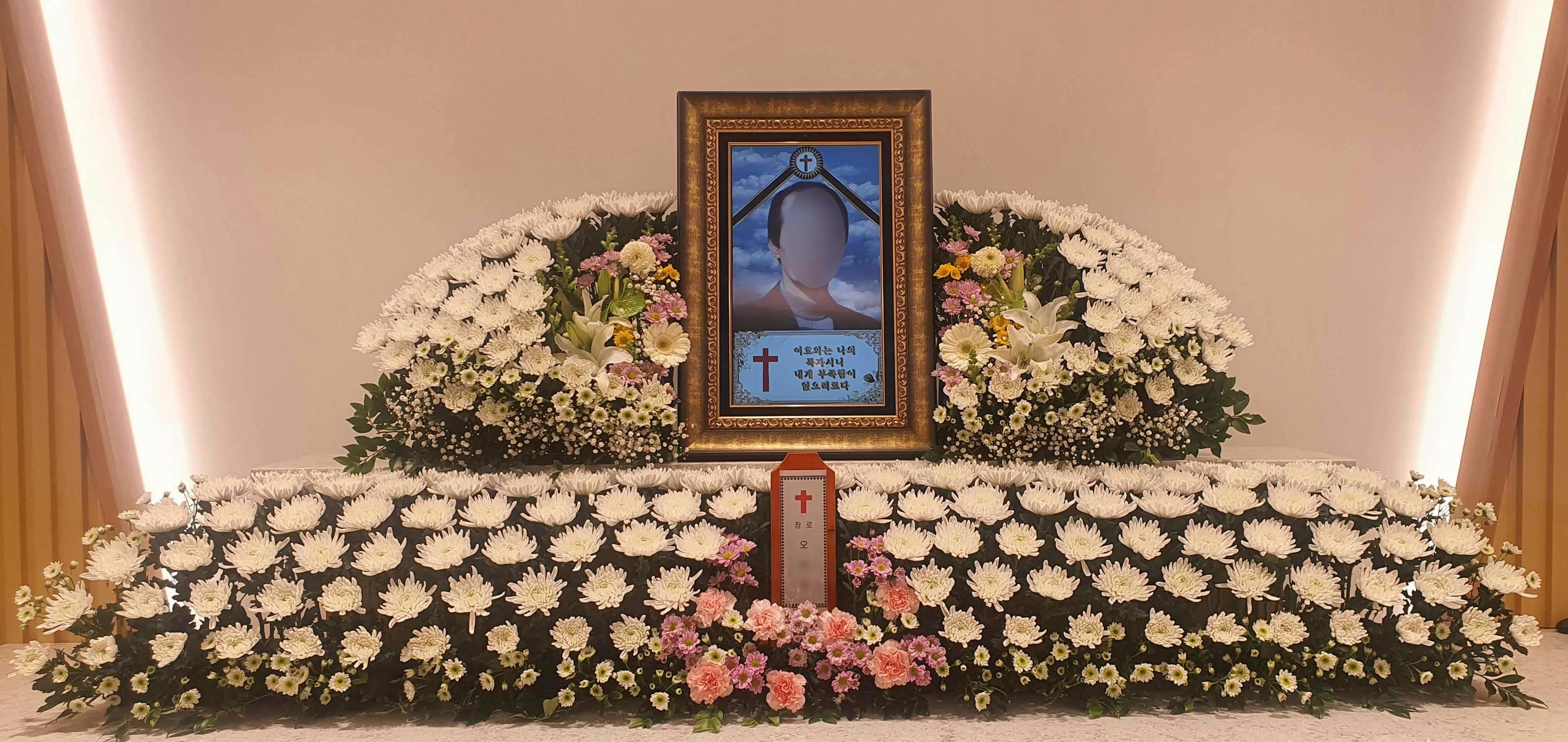 하얀 국화꽃으로 한 남자의 영정사진 주변이 장식되어 있는 모습.